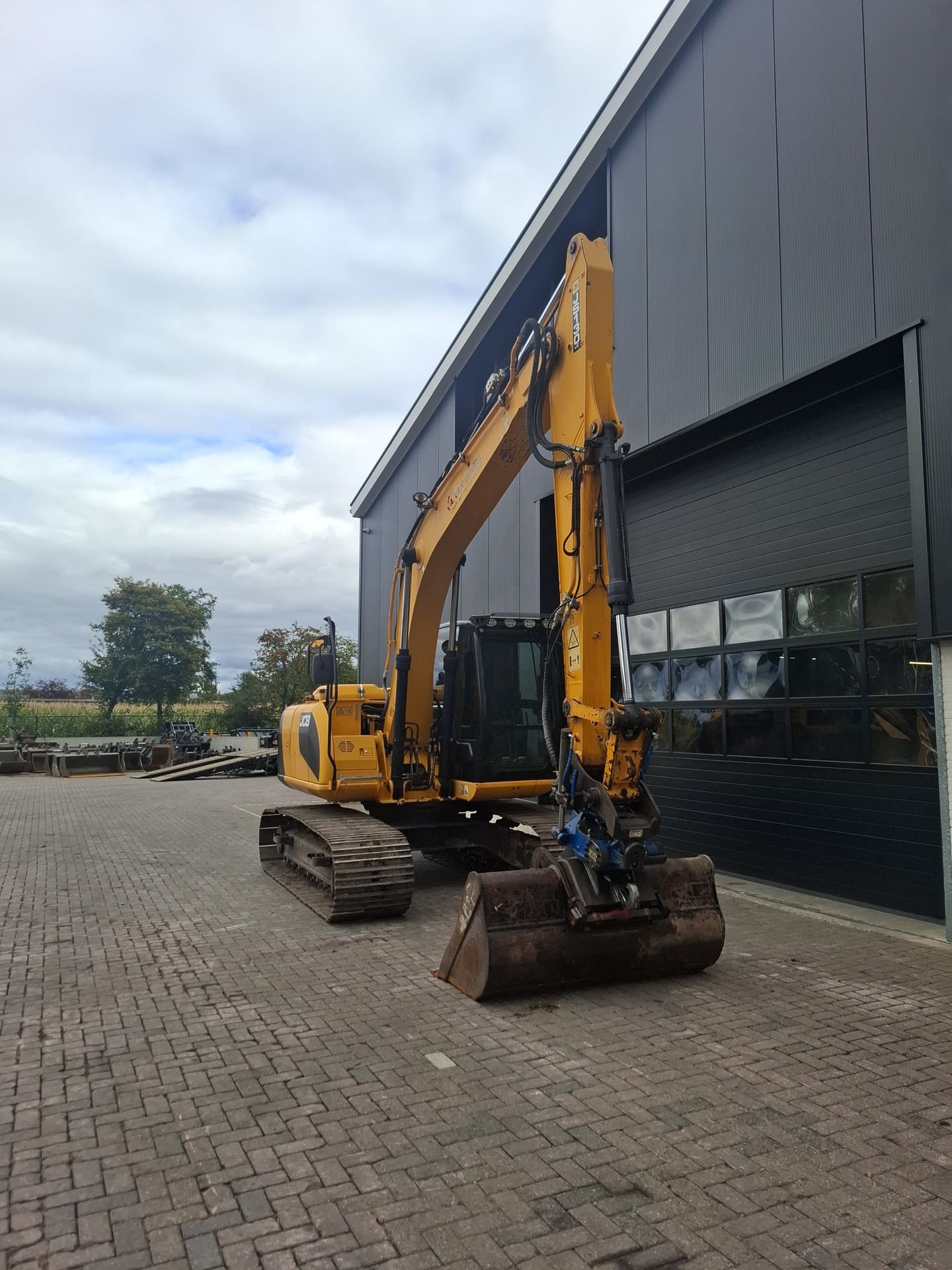 JCB JS130LC rupsgraafmachine schuin vooraanzicht bij de loods
